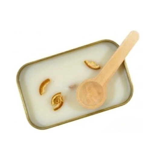 Overhead view of white scoopable wax in a gold tin topped with a few pieces of dried orange peel and a wooden scoop.