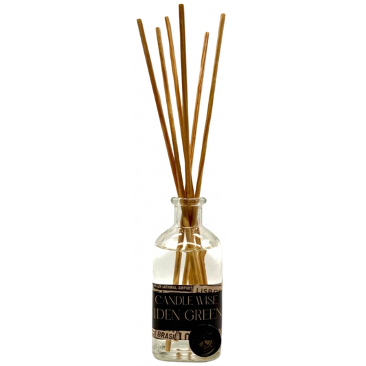 A clear glass reed diffuser bottle with a black label featuring the brand Candle Wise and the scent name IDEN GREEN in a serif font. Several light brown wooden reeds emerge from the narrow neck of the bottle.