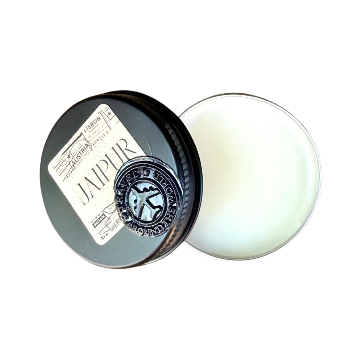 An open circular tin of white solid perfume with its black lid resting beside it. The lid features a vintage travel themed sticker with the word JAIPUR and a round black seal depicting an aeroplane surrounded by the text TRAVEL THE WORLD AROUND.