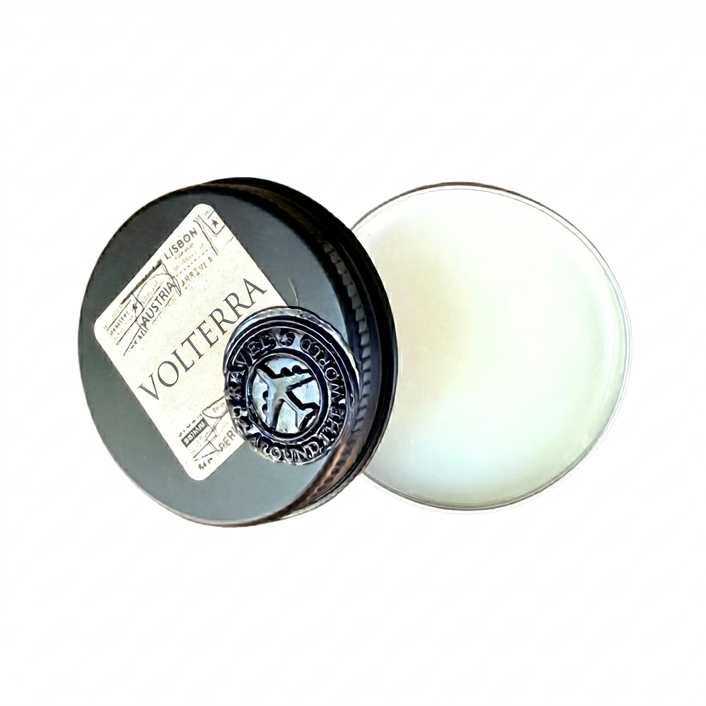 An opened circular black tin showing a natural wax based unisex solid perfume balm next to its lid. The lid features a vintage style Volterra travel stamp label and a metallic silver aeroplane seal.