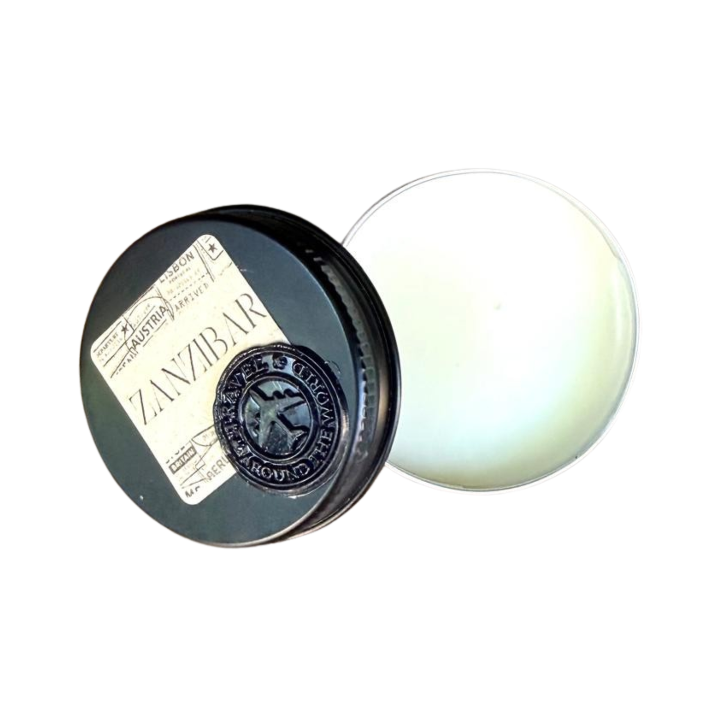 An open black round tin showing off-white solid perfume inside. The lid is placed to the left, decorated with a vintage style passport stamp sticker reading ZANZIBAR and a black circular wax seal showing an aeroplane icon.